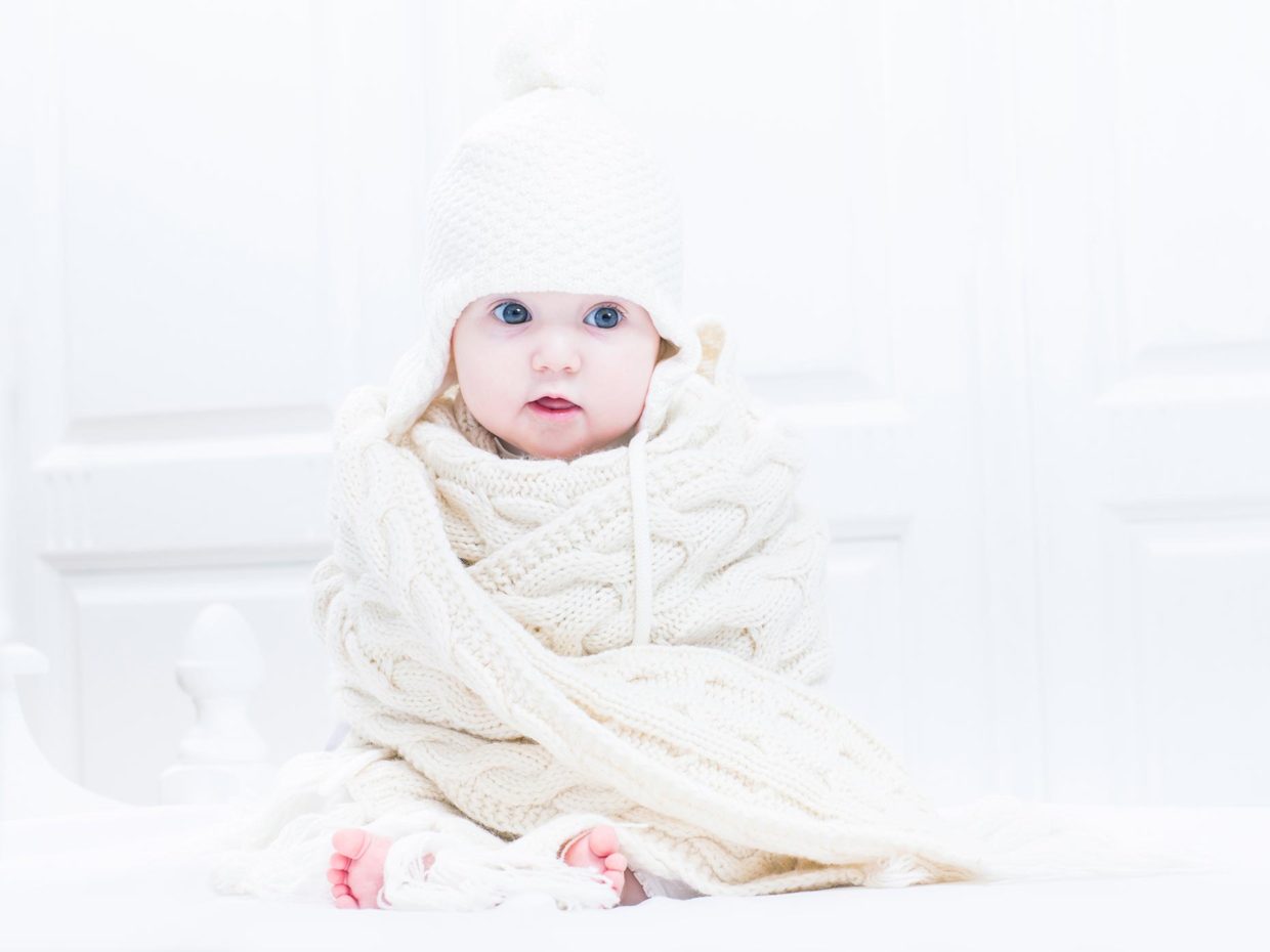 bambino avvolto in una coperta bianca con cappello di lana in testa