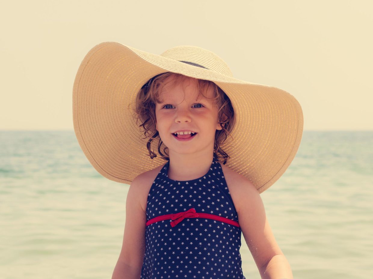 bambina con cappello di paglia a banda larga in spiaggia