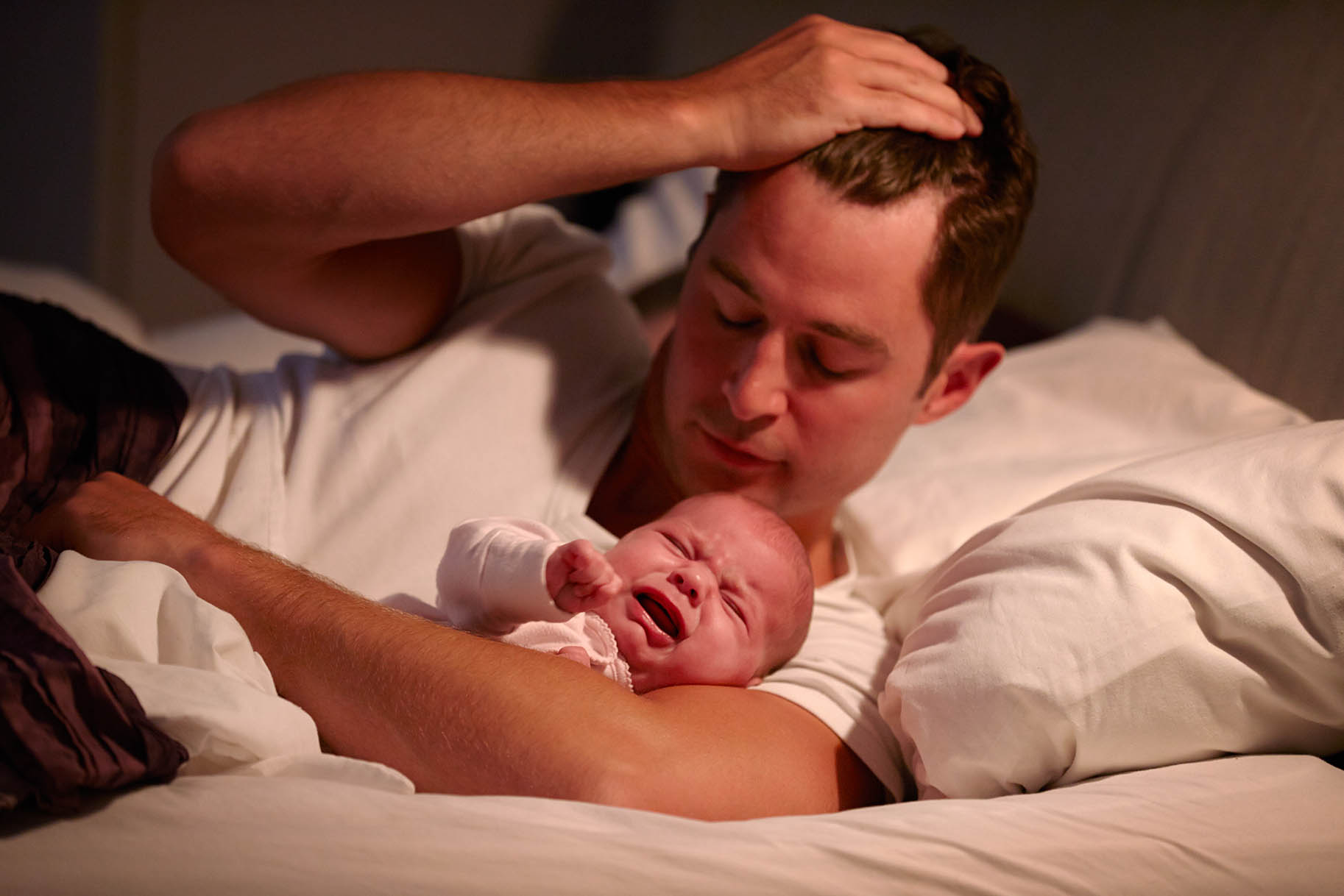 papà con mano nei capelli abbraccia nel letto il figlio che piange