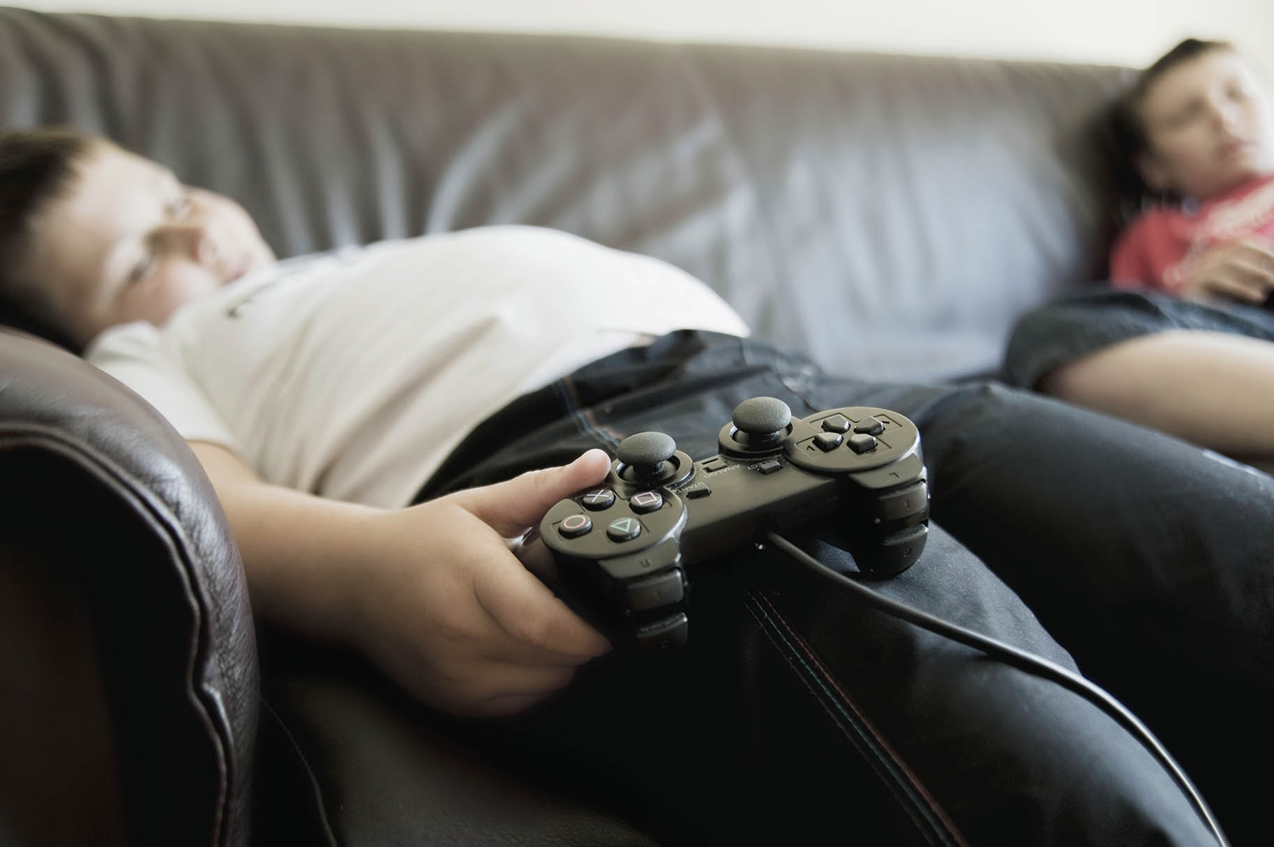 bambino sovrappeso coricato nel divano con joystick in mano