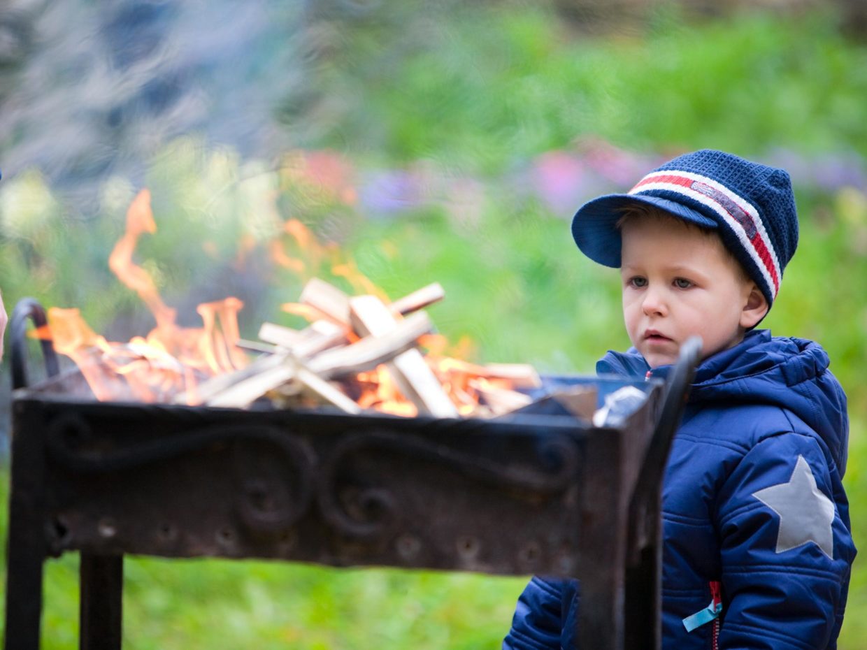 bambino con cappello osserva il fuoco della griglia