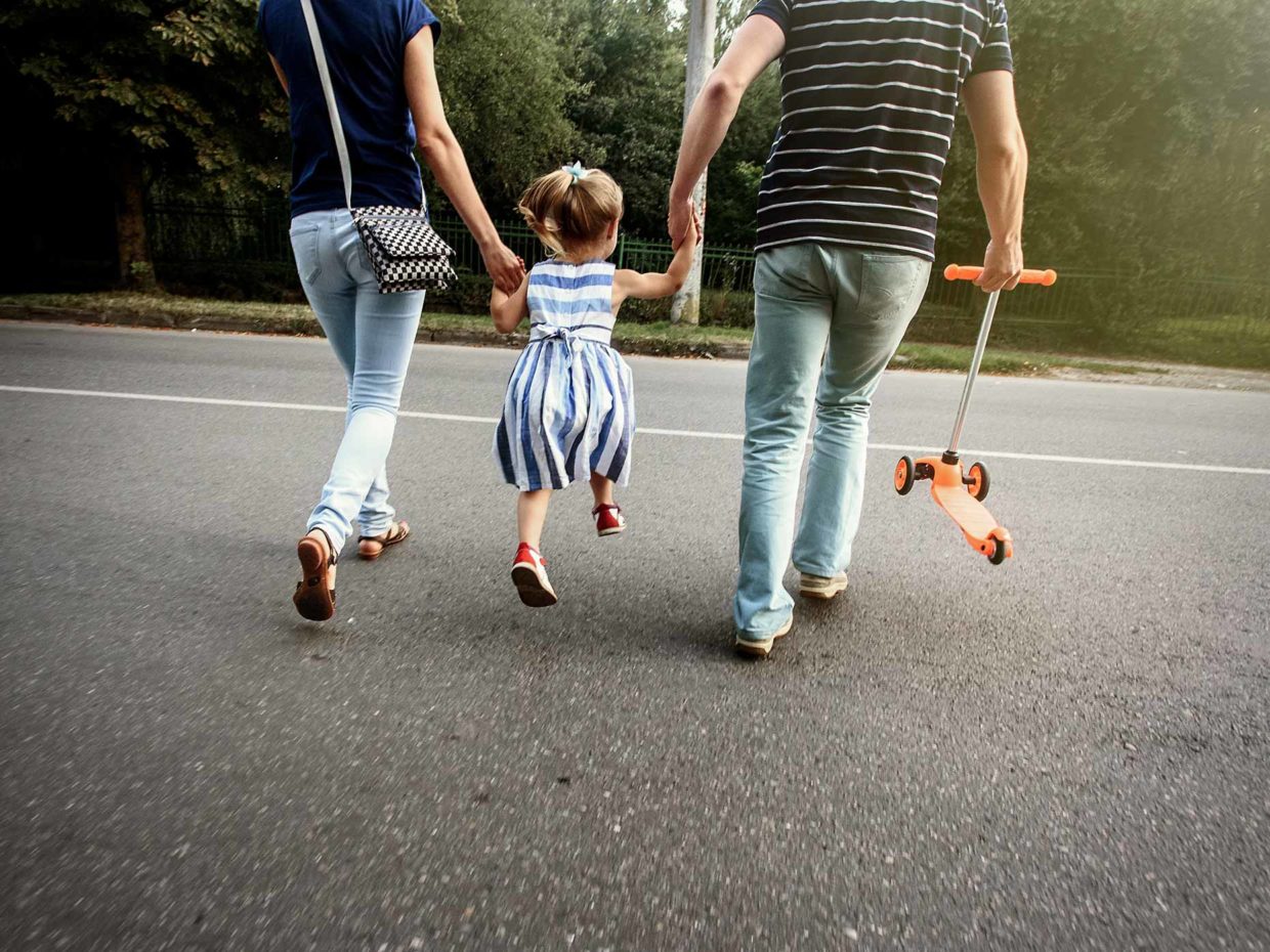 genitori danno la mano alla figlia per attraversare la strada