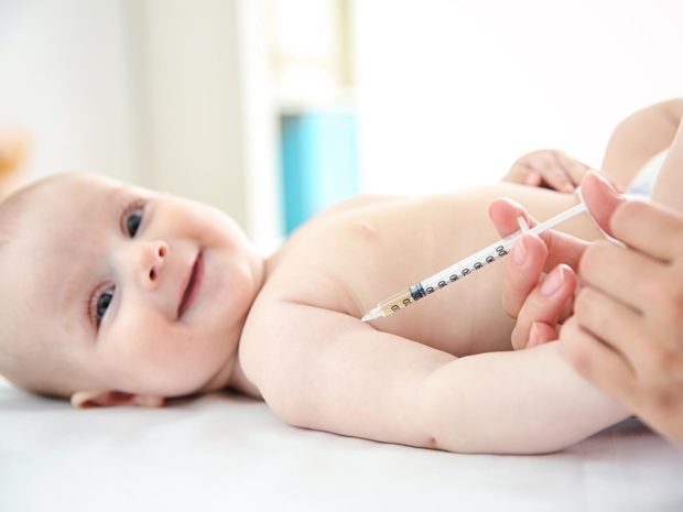 neonato sorridente mentre gli viene somministrata una iniezione