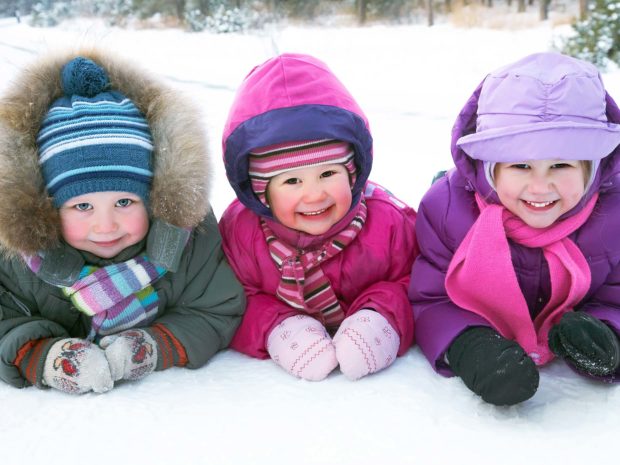 tre bambini sorridenti distesi sulla neve