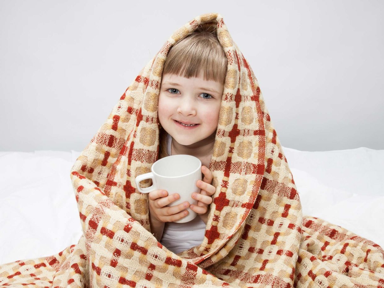 bambina sotto le coperte con tazza in mano