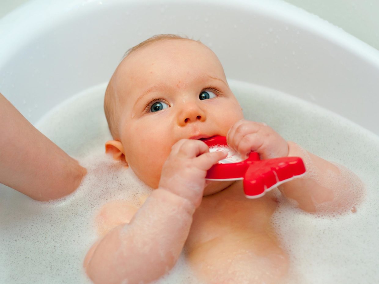 neonato fa il bagno mentre morde giocattolo rosso