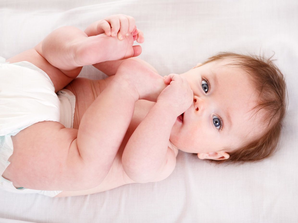 neonato con pannolino con un dito in bocca e con l'altra mano si tocca il piede