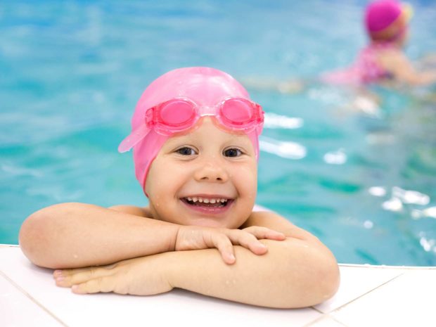 bambina appoggiata al bordo della piscina con cuffietka rosa