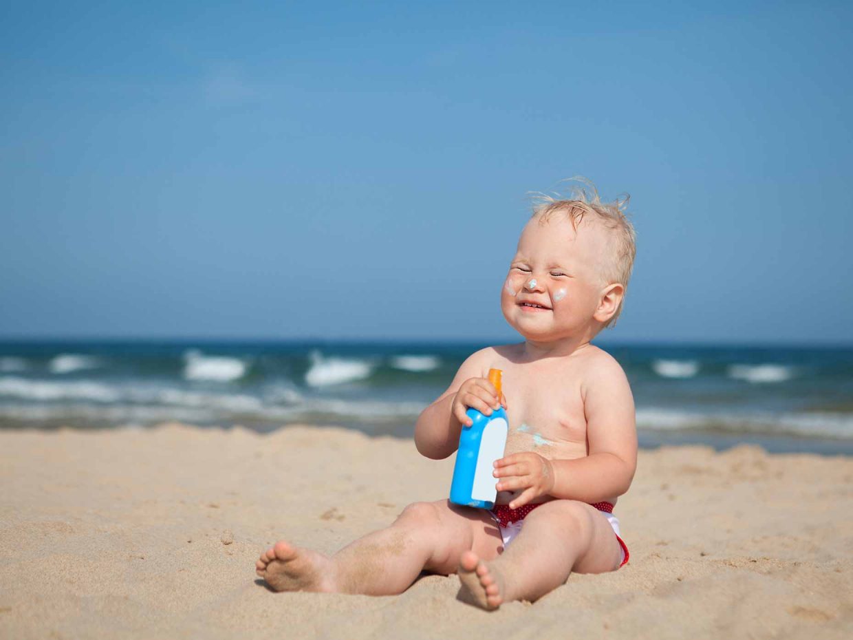 bambino sorridente seduto in spiaggia con la crema solare in mano