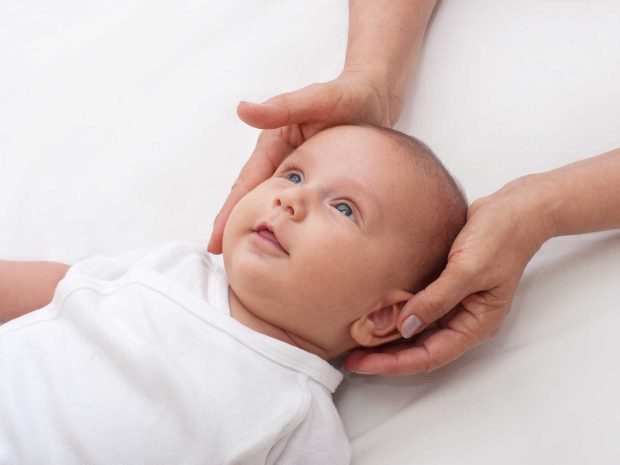 mani di adulto tengono dritta la testa di un neonato sdraiato