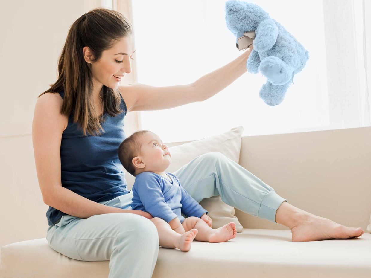 mamma tiene in alto orsetto di peluche azzurro mentre il bambino lo osserva