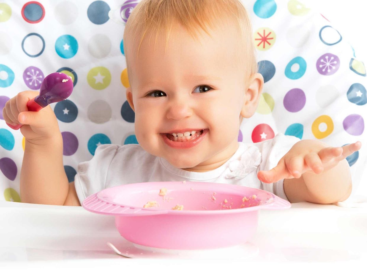 bambino piccolo sorride felice mangiando la pastina sul seggiolone