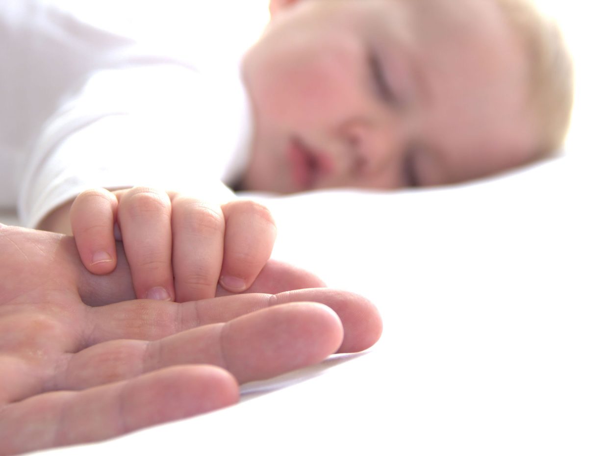 neonato dorme stringendo con la mano le dita del papà